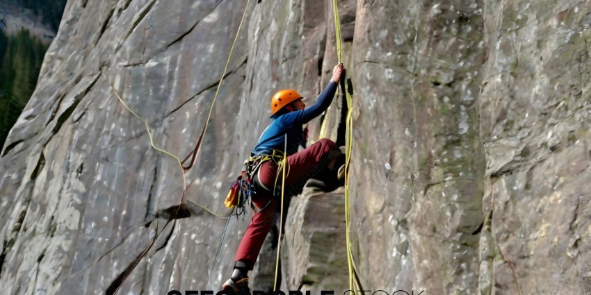 A climber in a blue shirt and red pants climbs a rock face