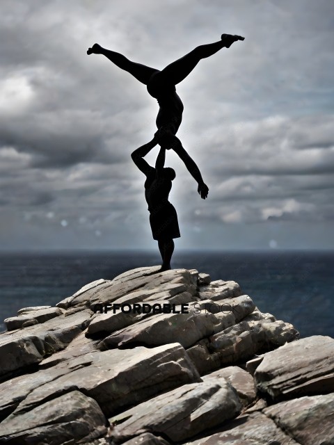 A man and woman are doing a handstand on a rocky cliff overlooking the ocean