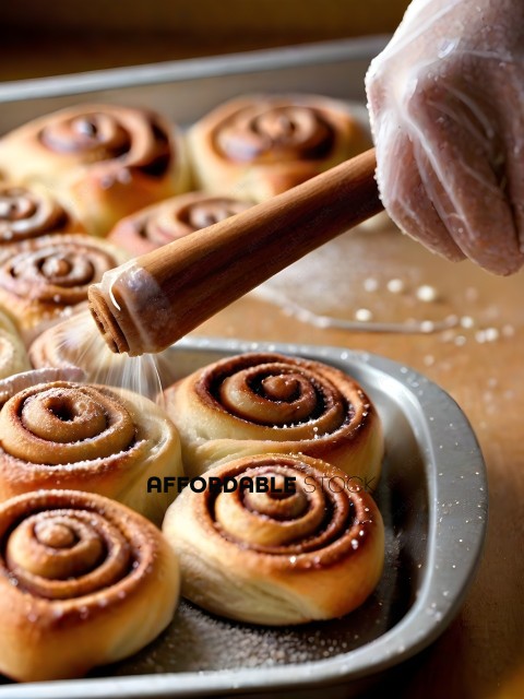 A person is pouring sugar on to a batch of freshly made cinnamon rolls