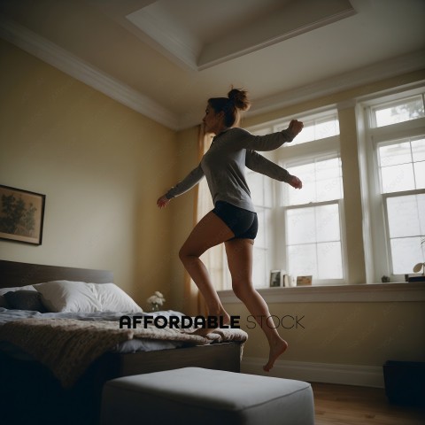 A woman in a grey shirt and black shorts jumping on a bed